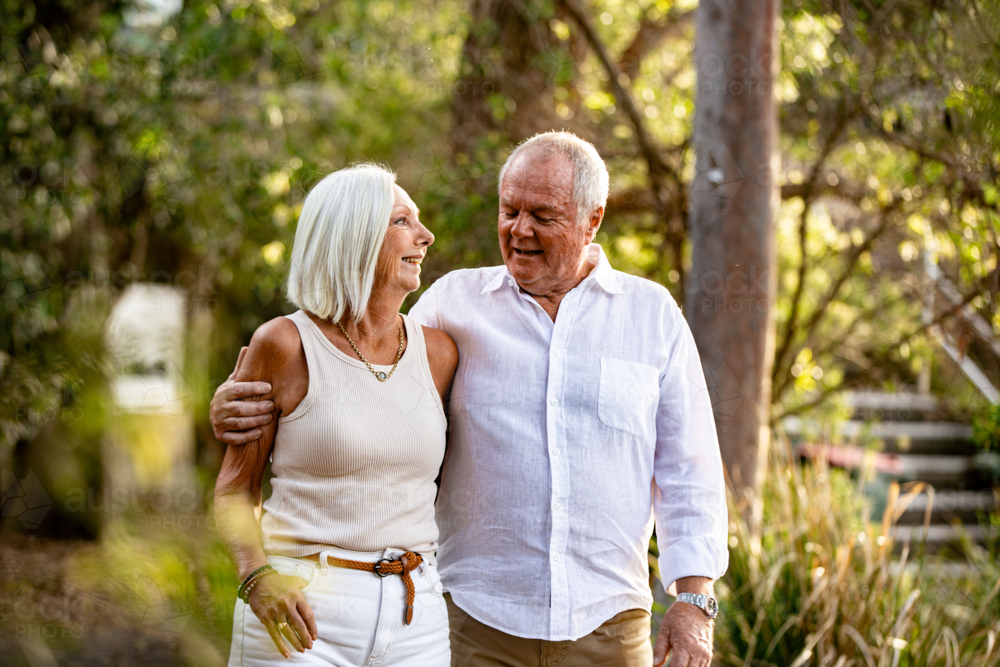 Senior couple walking in public park with arms over the other - Australian Stock Image