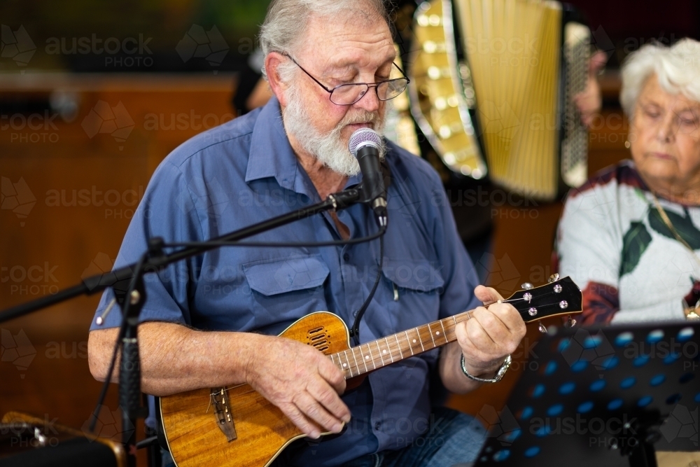 senior gentleman singing and playing a ukulele with lady looking on - Australian Stock Image