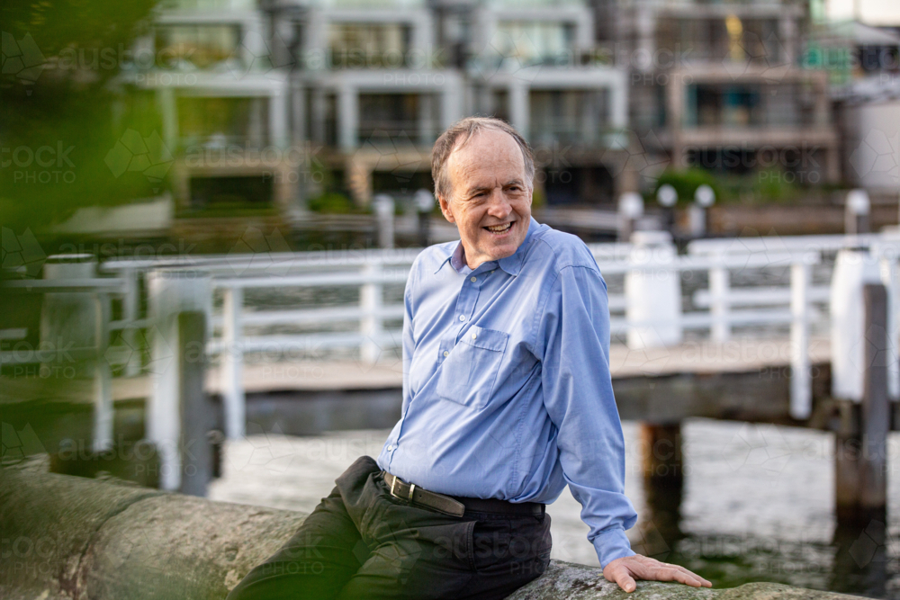 Senior man sitting on the stone ledge at the harbour. - Australian Stock Image