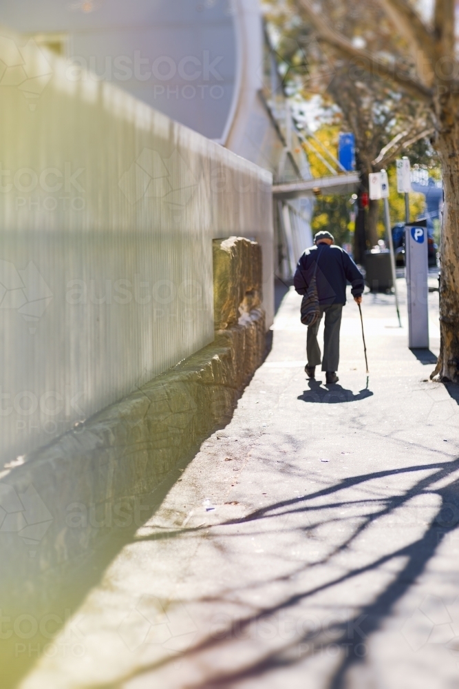 Senior man walking with cane away down sidewalk - Australian Stock Image