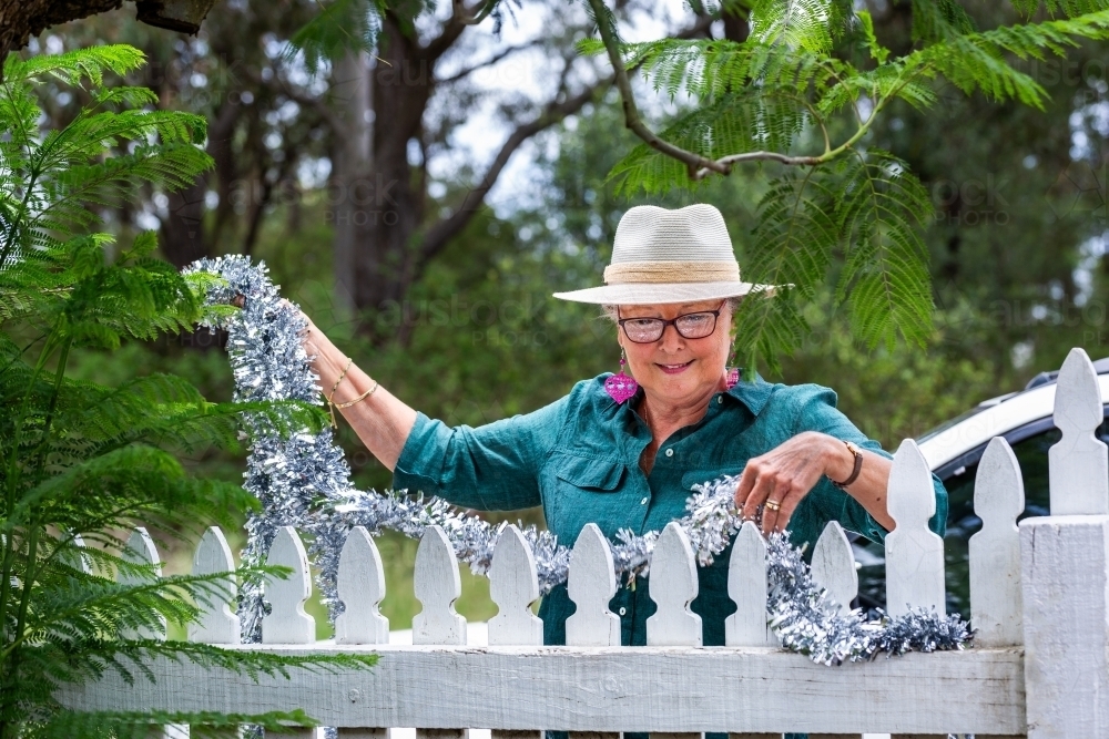 Senior woman in her sixties at Christmas standing beside white picket fence  - Australian Stock Image