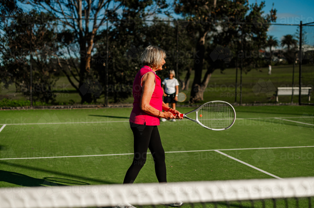 Senior woman in plays tennis outdoors in sunlight - Australian Stock Image