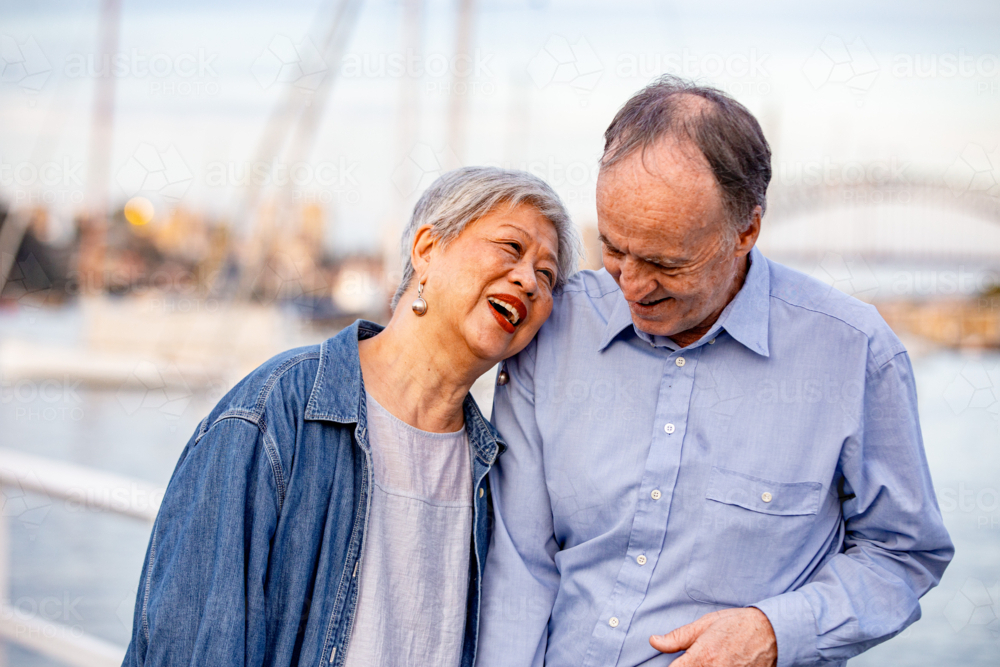 Senior woman leaning her head on mans shoulder while walking on the pier - Australian Stock Image