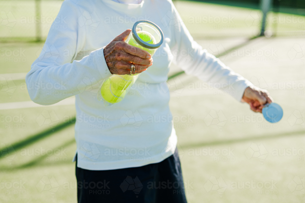 Senior woman opening a brand new can of tennis balls - Australian Stock Image