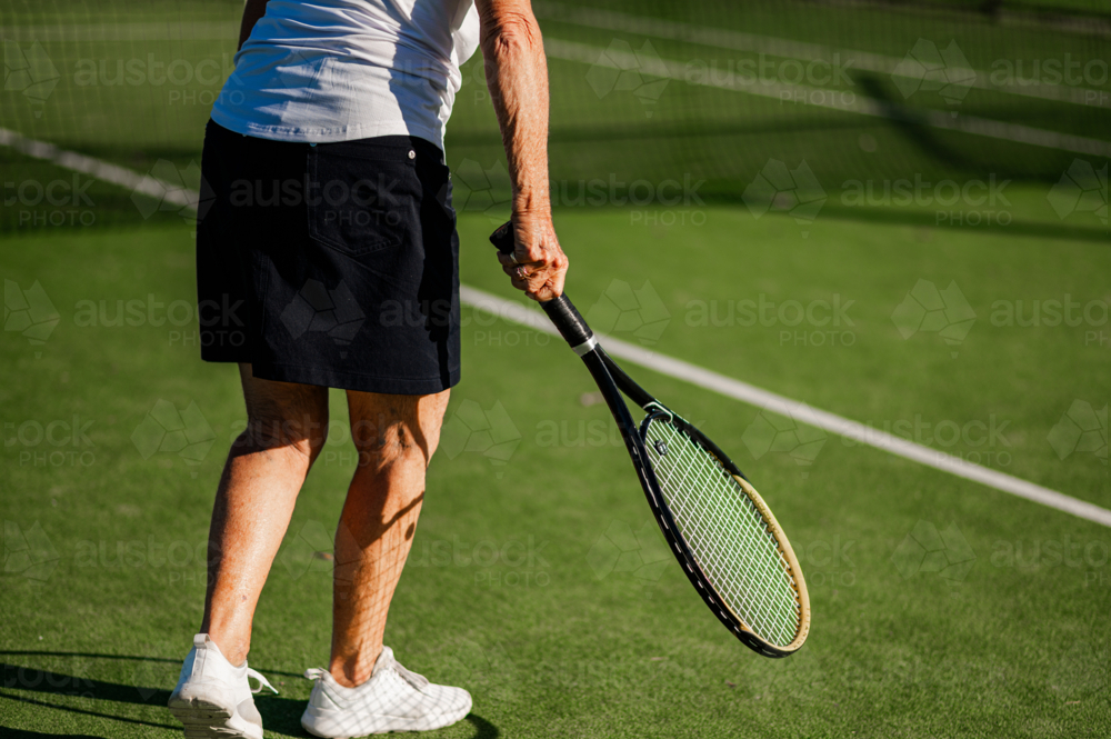 Senior woman prepares to serve on a tennis court - Australian Stock Image