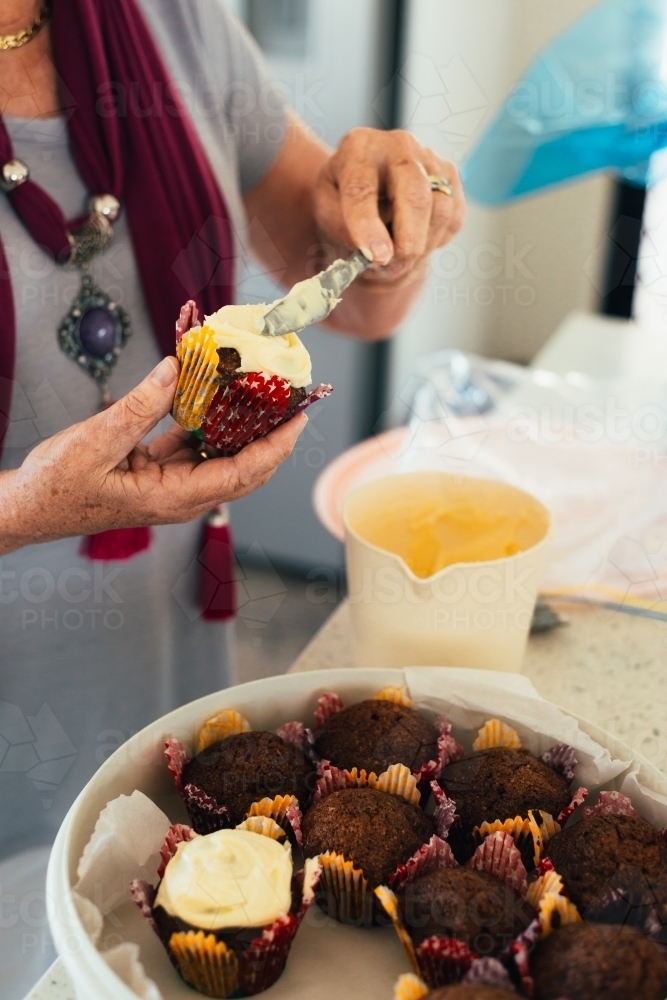 senior woman putting icing on cupcakes - Australian Stock Image