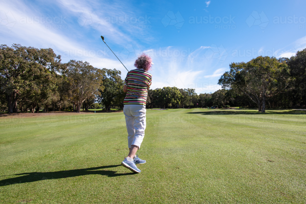 senior woman teeing off, wide shot of the golf course and blue sky - Australian Stock Image