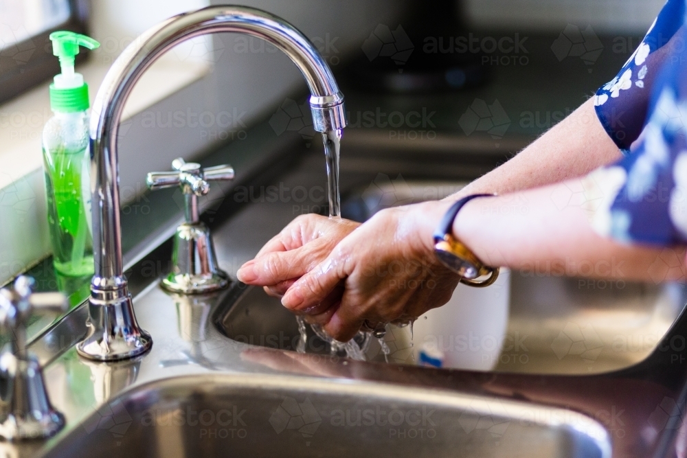 Image of senior woman washing hands with soap in the kitchen sink ...