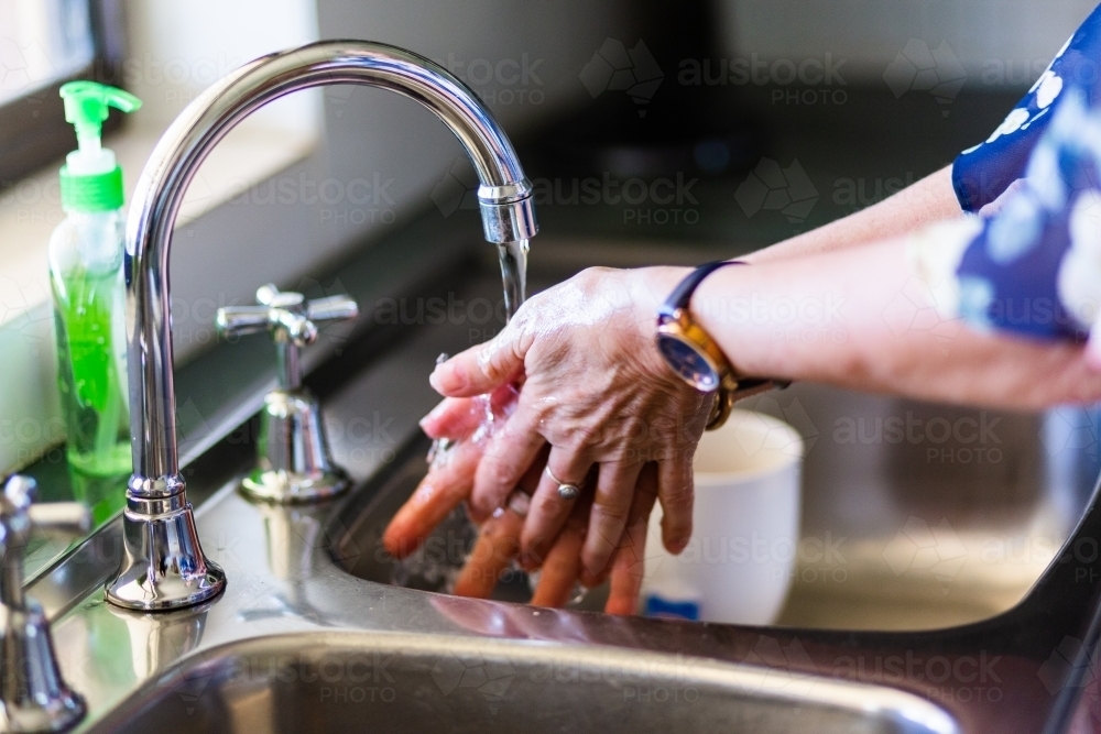 senior woman washing hands with soap in the kitchen sink - Australian Stock Image