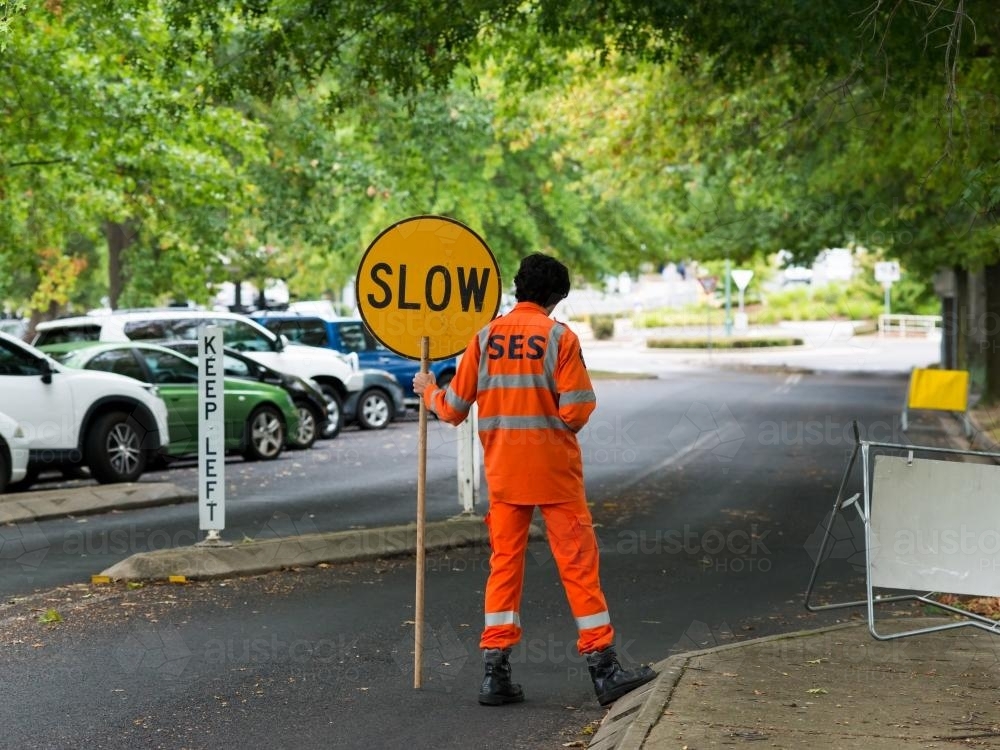 SES Volunteer in an orange suit holding a "SLOW" sign - Australian Stock Image