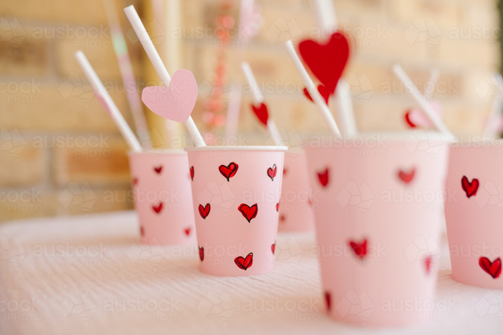 Set of paper cups with small red heart designs and straws. - Australian Stock Image
