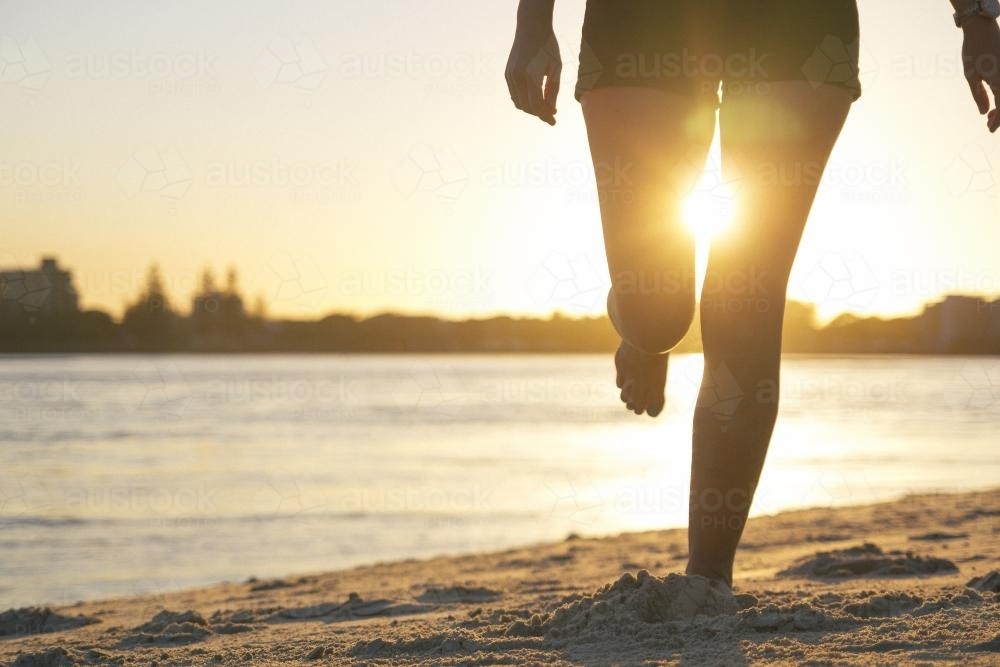Setting sun shining through legs of person standing on the beach - Australian Stock Image