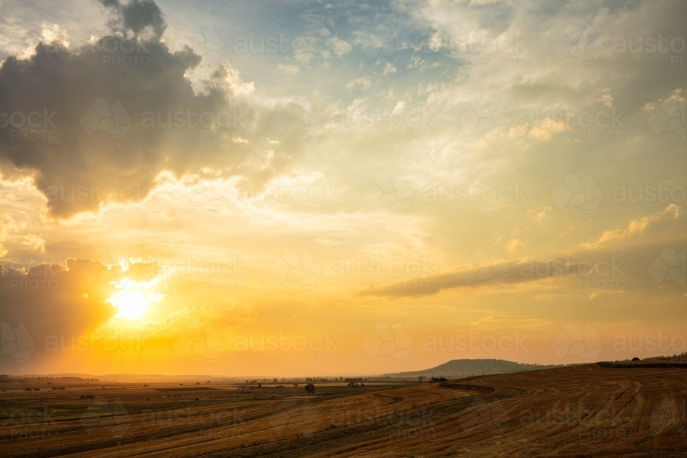 Setting yellow sun through cloud over a rural area of Queensland - Australian Stock Image