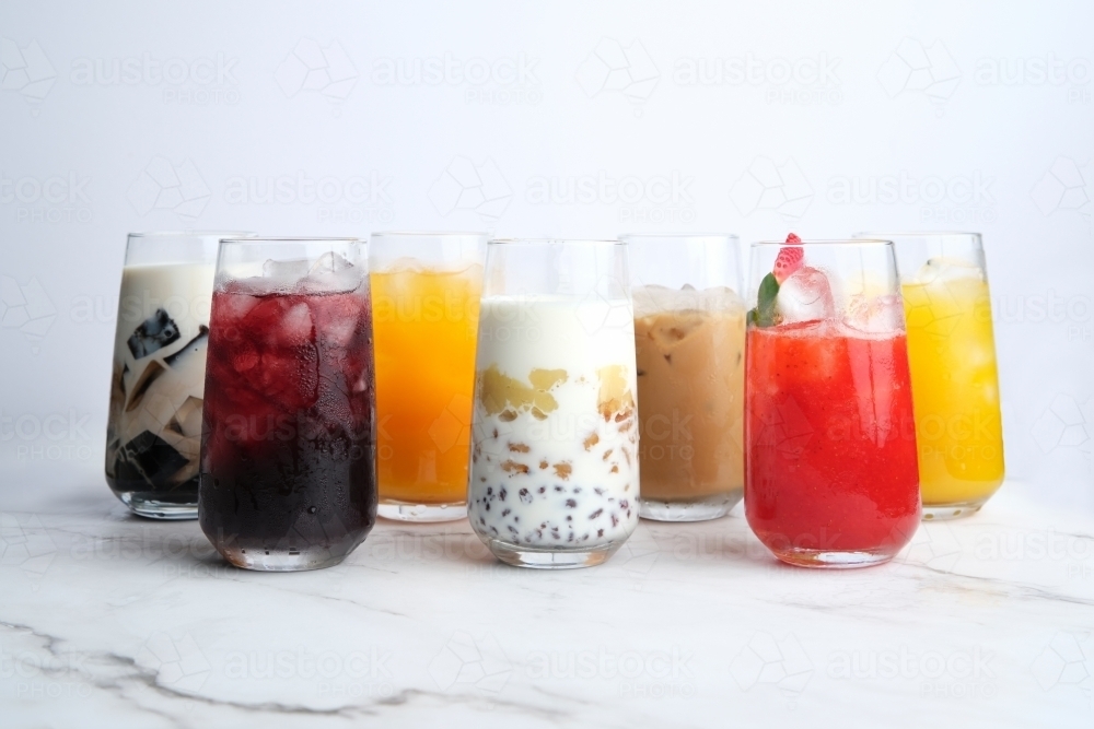 Seven Different kinds of colorful juice in a tall glass served on a white quartz counter top - Australian Stock Image
