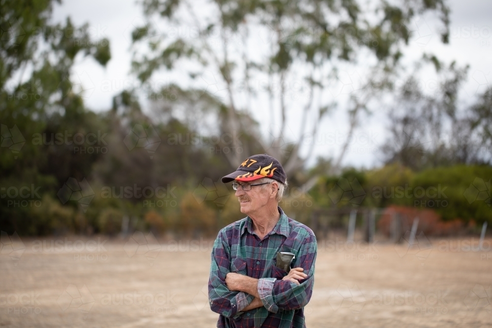 seventy-year-old man with arms crossed outdoors - Australian Stock Image