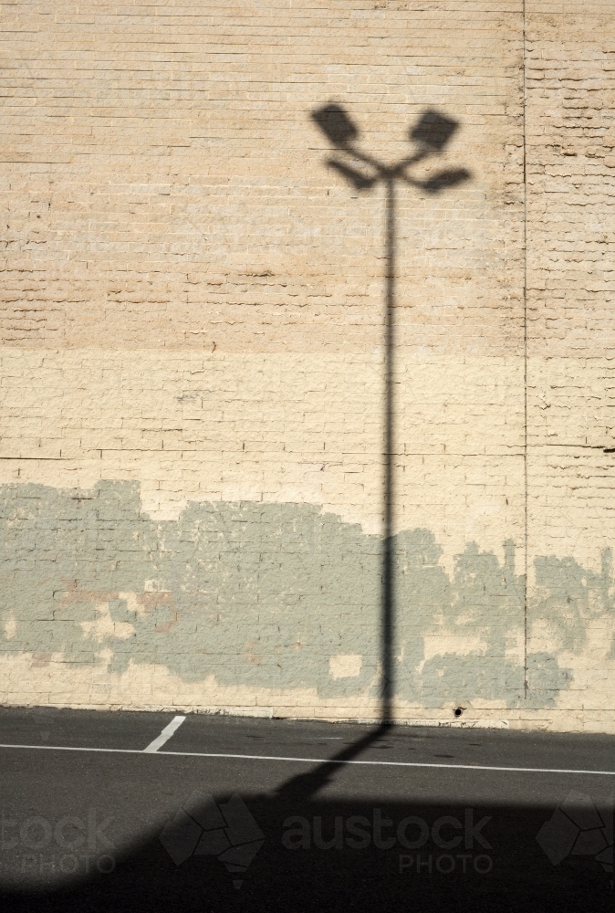 Shadow of a street lamp against a light brick wall - Australian Stock Image