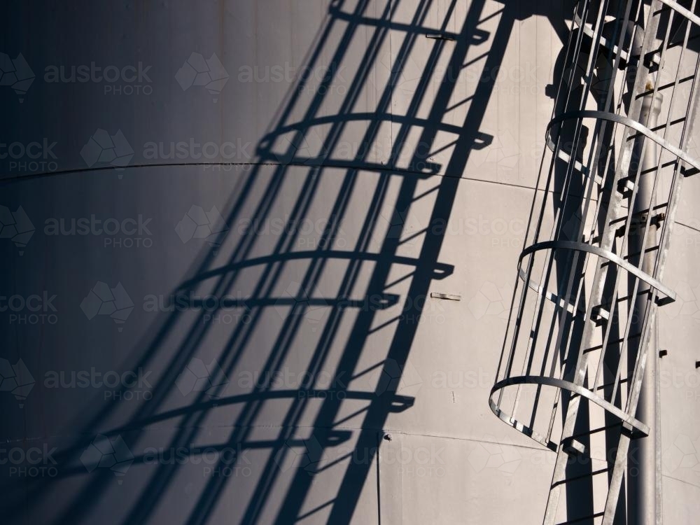 Shadow of stairway up the side of a industrial storage tank - Australian Stock Image