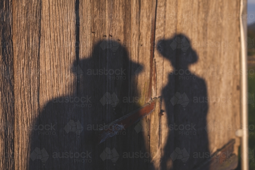 Shadow of two people against rustic wooden wall - Australian Stock Image
