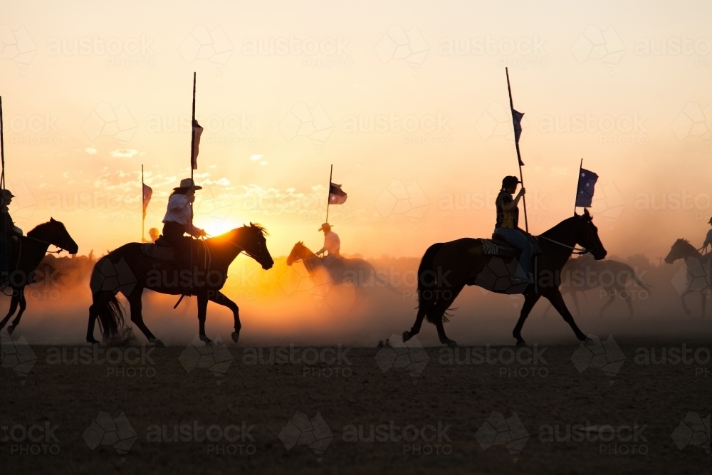 Shadows and silhouettes of horses and riders with australian flags on dust at sunset - Australian Stock Image