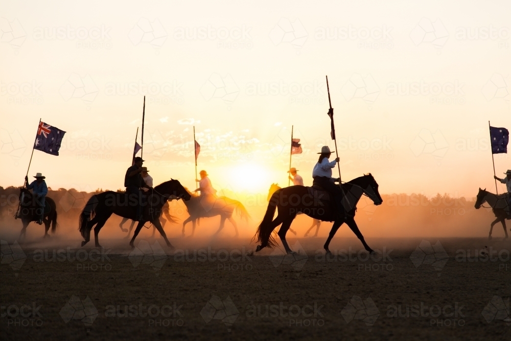 Shadows and silhouettes of horses and riders with australian flags on dust at sunset - Australian Stock Image