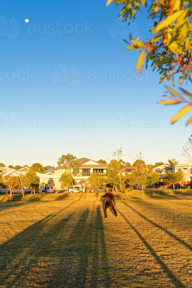 Shadows of people watching a man playing with kids frisbee at a park at sunset - Australian Stock Image