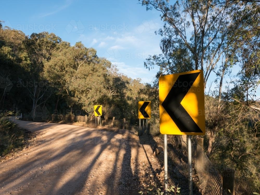 Sharp bend signs on narrow dirt mountain road - Australian Stock Image