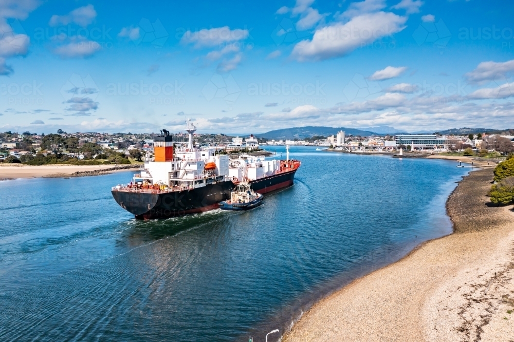 Ship arriving in port with tug boat alongside - Australian Stock Image
