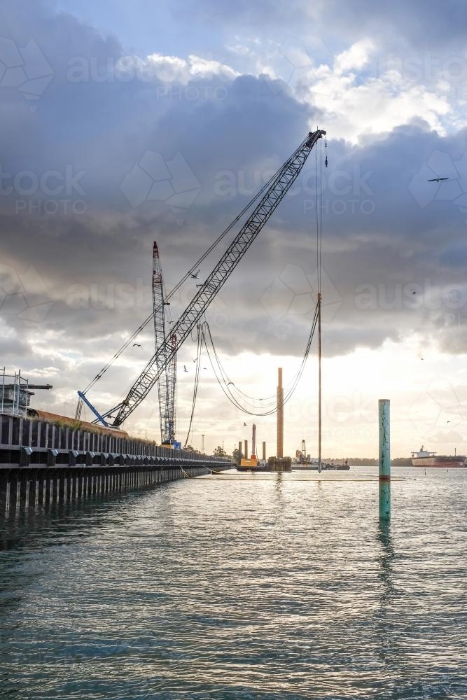ship loading dock and cranes with sun shining through clouds - Australian Stock Image