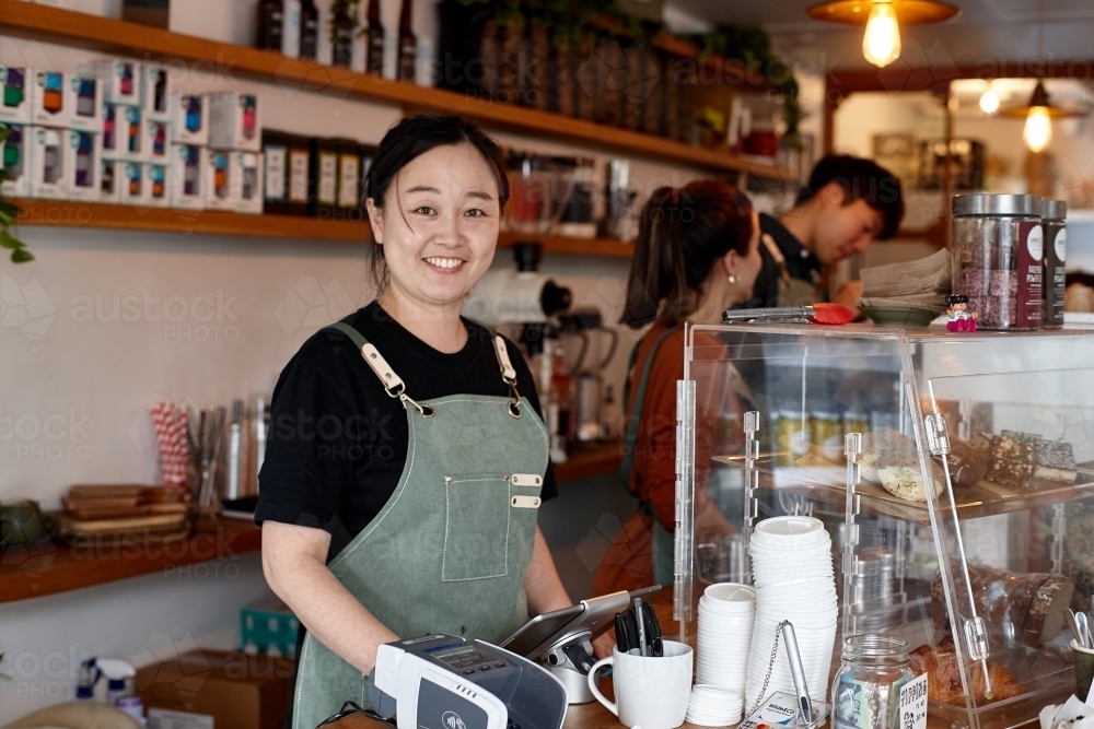 Shop owner smiling whilst working inside coffee shop - Australian Stock Image