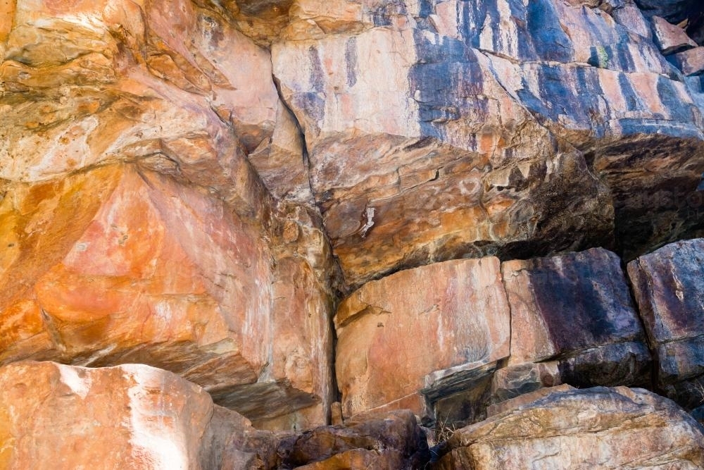 Shot of rocky cliff face with crevices and layered orange and dark rock - Australian Stock Image