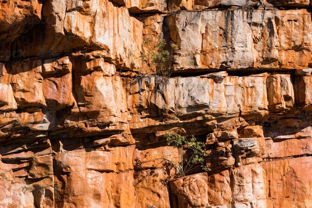 Shot of rocky cliff face with crevices and layered orange and dark rock - Australian Stock Image