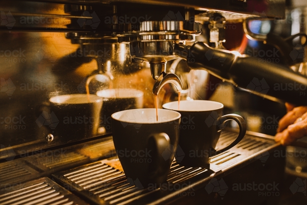 Shots of coffee dripping from machine into cups - Australian Stock Image