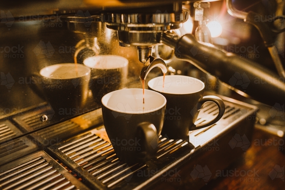 Shots of coffee dripping from machine into cups - Australian Stock Image