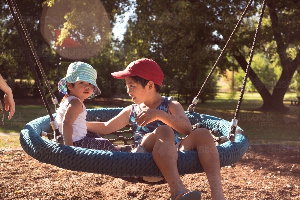 siblings enjoying a ride on a swing - Australian Stock Image