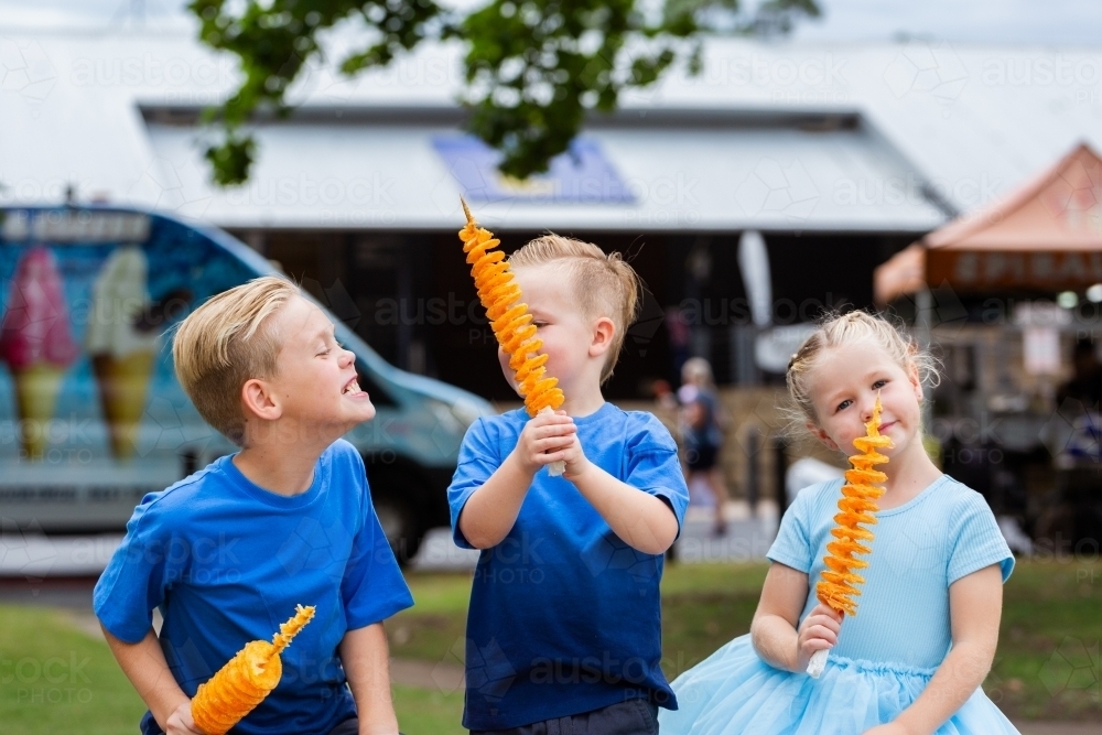Siblings sitting together with potato spiral chips to eat at local event - Australian Stock Image