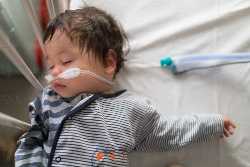 Sick mixed race year old boy asleep being treated with oxygen therapy in Children's Hospital ward - Australian Stock Image