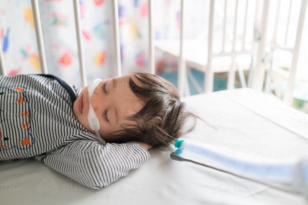 Sick mixed race year old boy asleep being treated with oxygen therapy in Children's Hospital ward - Australian Stock Image