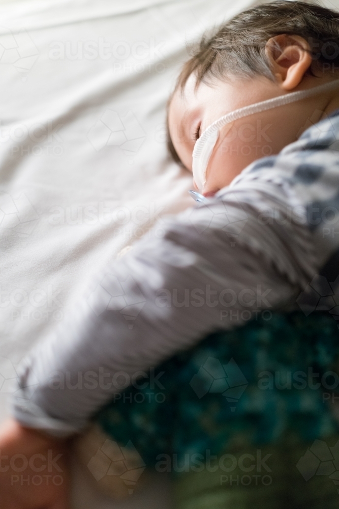 Sick mixed race year old boy asleep being treated with oxygen therapy in Children's Hospital ward - Australian Stock Image