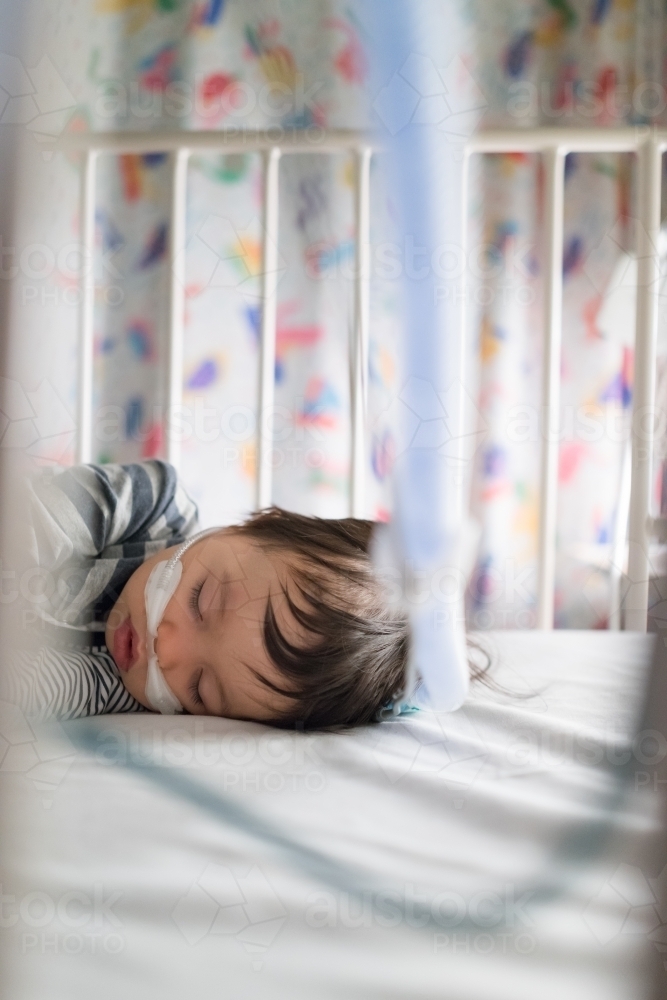 Sick mixed race year old boy asleep being treated with oxygen therapy in Children's Hospital ward - Australian Stock Image