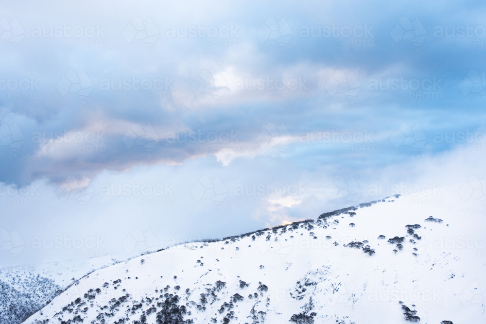 Side of hill covered in snow with pink and blue clouds overhead - Australian Stock Image