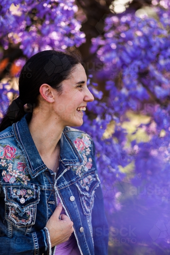 Side on profile of happy woman laughing in spring with background of purple jacaranda flowers - Australian Stock Image