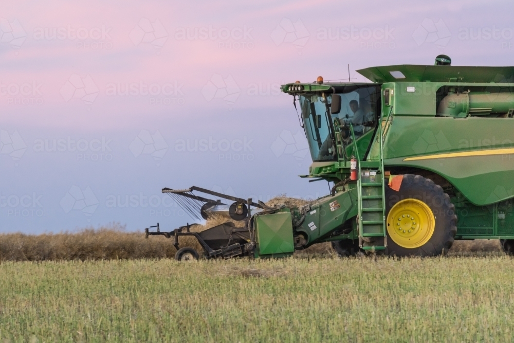 Side on view of a harvester working in a paddock at twilight - Australian Stock Image