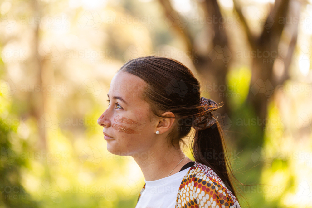 Side profile of teen aboriginal girl looking up wearing traditional ochre face paint - Australian Stock Image