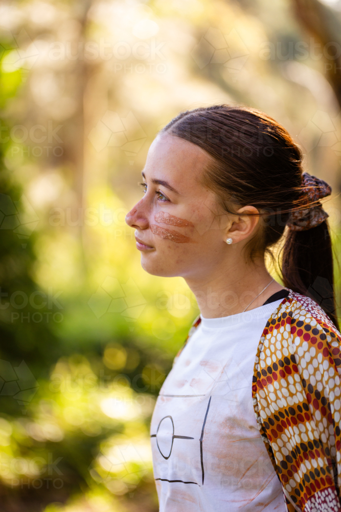 Side profile of teen aboriginal girl looking up wearing traditional ochre face paint - Australian Stock Image