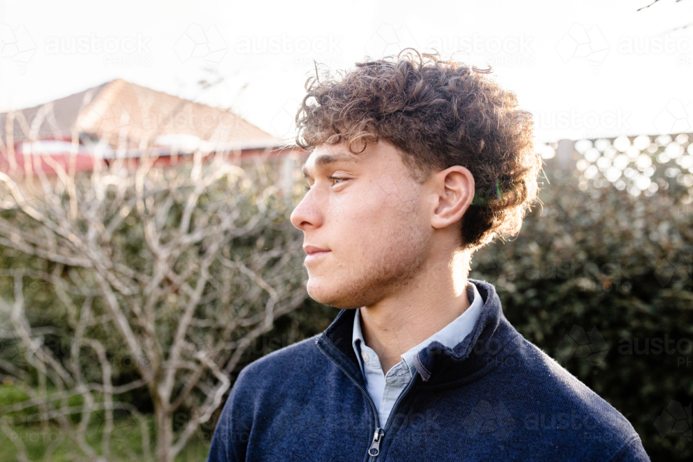 Side profile of teenage boy with curly hair standing outdoors in the garden - Australian Stock Image