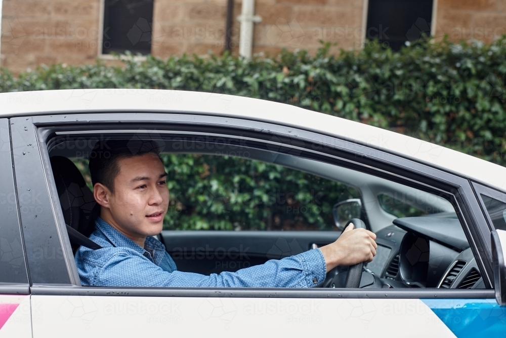 Side shot of Asian man driving in car - Australian Stock Image