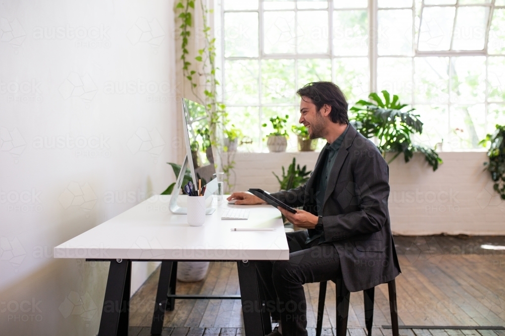 Side view of a happy business man working at a desk in a studio space - Australian Stock Image