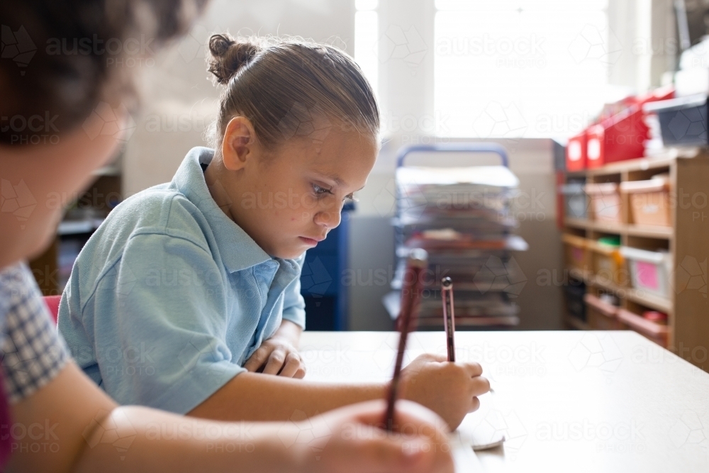 Side view of an indigenous primary school student writing in a classroom - Australian Stock Image