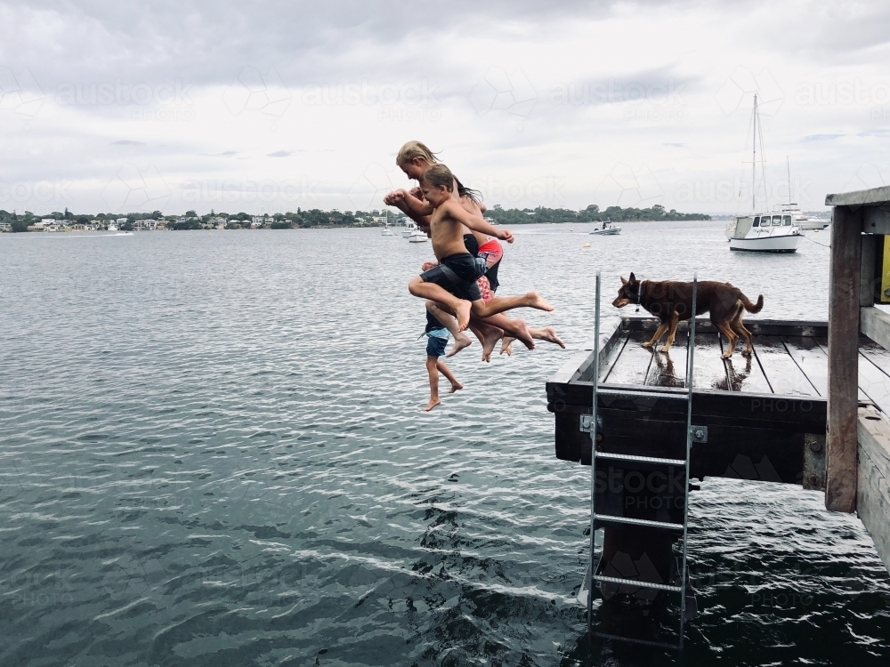 Side view of kids jumping off a pier into the water - Australian Stock Image