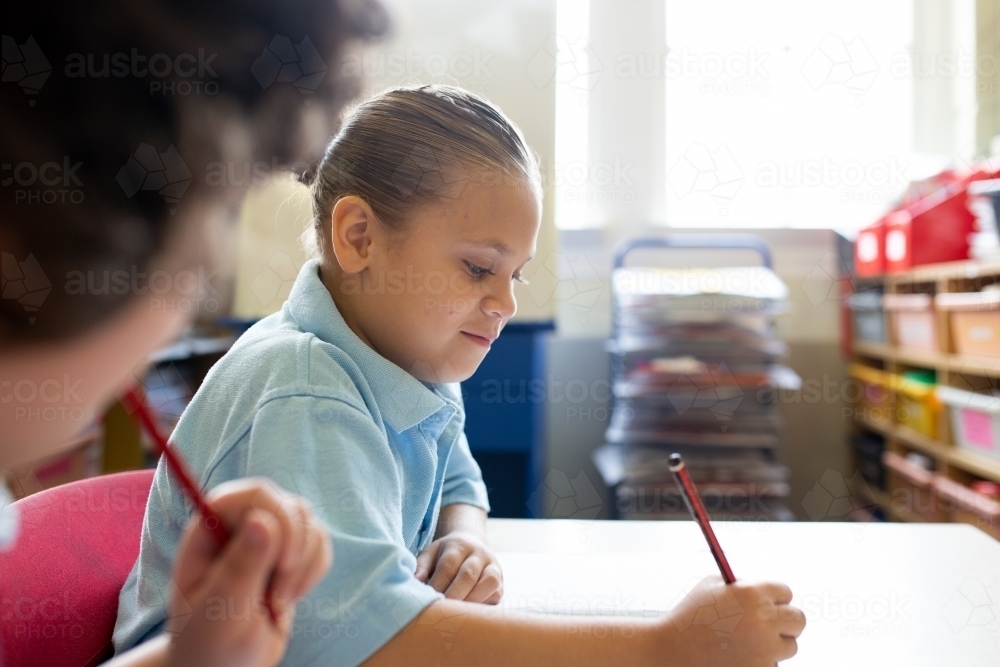 Side view of two primary school girls writing in a classroom - Australian Stock Image